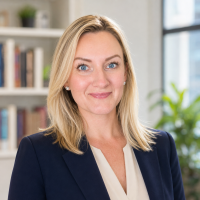 Head-and-shoulders portrait of a smiling blonde woman in a navy blazer in an office setting with bookshelves in the background
